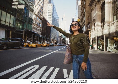 Pretty mixed race woman calling yellow taxi cab in Manhattan, New York. Inspiring photo of stylish student girl in the big city.