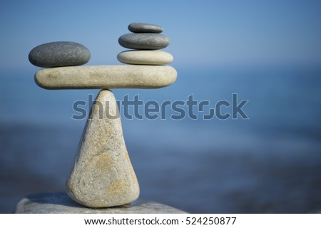 Balance of stones. To weight pros and cons. Balancing stones on the top of boulder. Close up. Balance of stones on a blue sky background with a copy space. Scales. Stones balance, sustainability. Royalty-Free Stock Photo #524250877