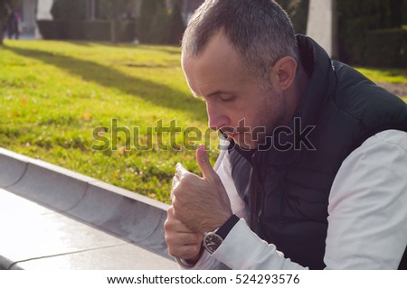 A man is lighting up a cigarette outdoors. Focus point is on the cigarette. Handsome man lighting up cigarette on urban city street. City fashion.