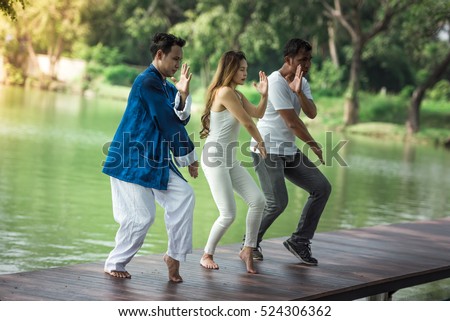 Group of young people practicing traditional Tai Chi Chuan, Tai Ji  and Qi Gong for fighting match together in the park on the lake background, traditional chinese martial arts concept. Royalty-Free Stock Photo #524306362