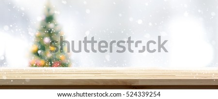 Wood table top on blur Christmas tree background in snowfall, panoramic banner