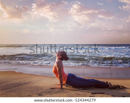 Vintage retro effect hipster style image of Yoga outdoors on beach - woman practices Ashtanga Vinyasa yoga Surya Namaskar Sun Salutation asana Urdhva Mukha Svanasana - upward facing dog pose on sunset