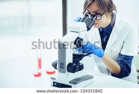 Young scientist looking through a microscope in a laboratory. Young scientist doing some research. Royalty-Free Stock Photo #524351842