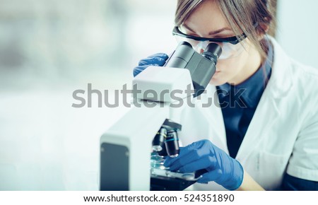 Young scientist looking through a microscope in a laboratory. Young scientist doing some research. Royalty-Free Stock Photo #524351890