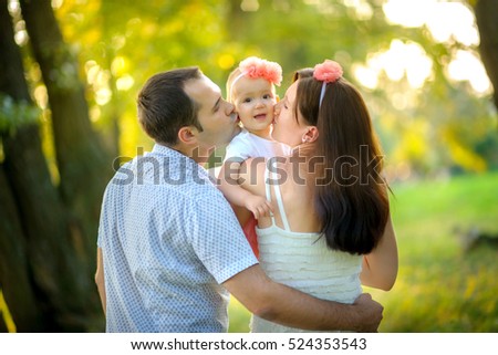 happy family walks in the park, embrace and together kiss the daughter, on a background a bright sunset