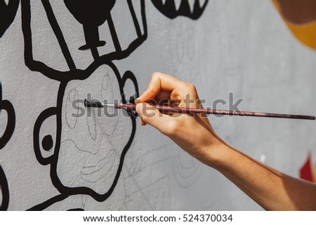Young woman painting a picture on the wall, street artist, brush in hand and black paint