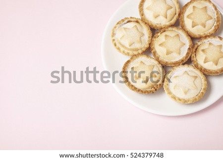 A plate full of freshly baked mince pies on a pastel pink background with blank space at side