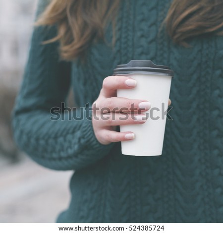 Pretty young woman in stylish green sweater holding cup in hands. Warm soft cozy image. Details. Drinking take away coffee. Breakfast on the go. Instagram style toned image