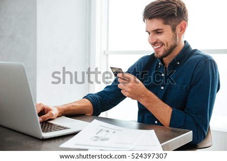 Photo of young man holding a credit card and typing. Online shopping on the internet using a laptop. Looking at the laptop.