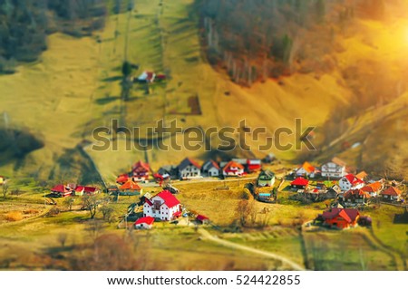 a small village in the valley in the highlands. Houses with red roofs and around the forest and mountain slopes. Effect of toy houses. Sunlight gently illuminating the area around. Fabulous picture.
