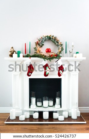A picture of a great white fireplace decorated with many candles, green pine wreaths and bright red Christmas socks.