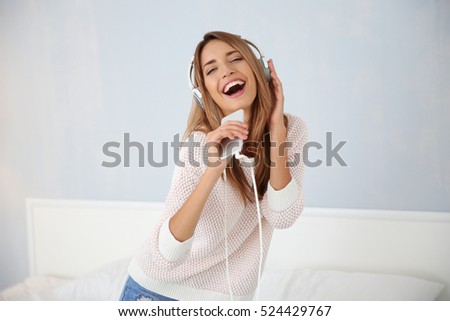 Beautiful young woman listening to music in headphones at home