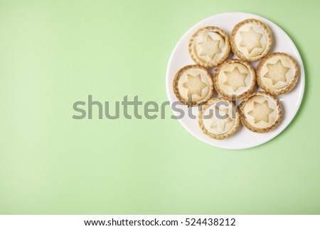 A plate full of freshly baked mince pies on a pastel green background with empty space at side