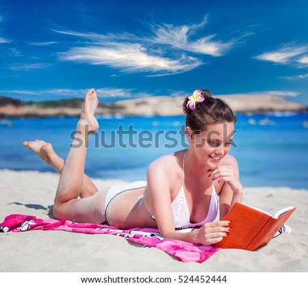 Pretty brunette woman is reading a book while lying on a beach