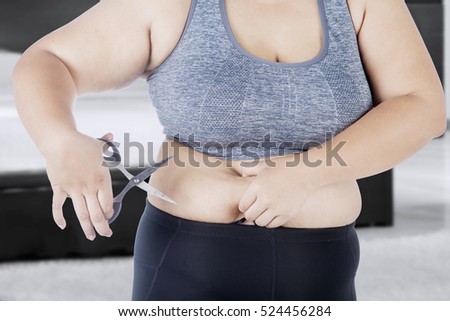 Picture of woman holds her big belly with a scissor while standing at home 
