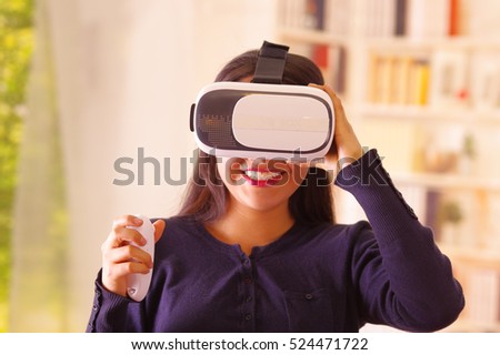 Young brunette woman wearing virtual reality goggles experiencing future technology, interacting and smiling while playing, domestic background,vr concept