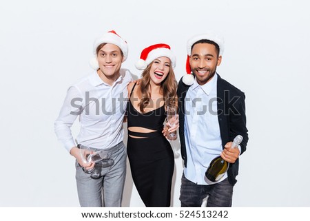 Three happy friends in santa claus hats with bottle of champagne over white background