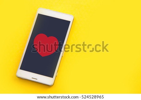 white smart phone and red heart on yellow background.Concept of love connection