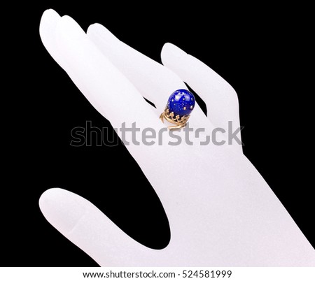 Golden ring decorated with the dark blue murano glass bead on the white ghostly hand against the black background