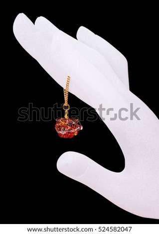 Red murano glass pendant with a golden chain hanging off the white ghostly hand against the black background