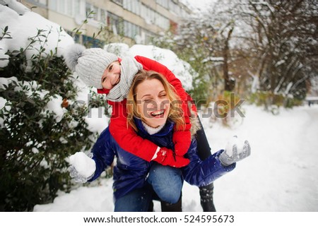 Mother and the daughter cheerfully spend time in winter day. They walk in the snow-covered park. In hands at the woman snowballs. She in someone aims. Girl embraces mother. Both laugh. It is snowing.