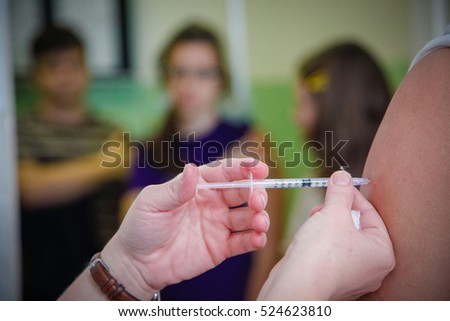 Nurse administering vaccination to students arms in a high school. Royalty-Free Stock Photo #524623810