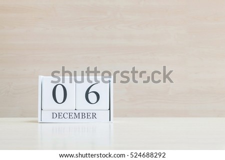 Closeup surface white wooden calendar with black 6 december word on blurred brown wood desk and wood wall textured background with copy space , selective focus at the calendar