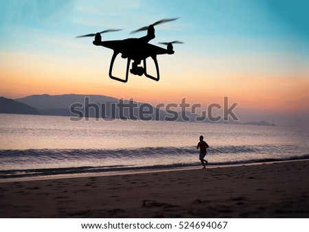 Hovering drone taking pictures of runner at the beach, sunset