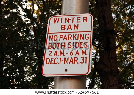 Parking ban in winter time road sign on roadside in front of trees.