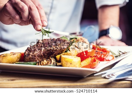 Chef in hotel or restaurant kitchen cooking only hands. Prepared beef steak with vegetable decoration.  Royalty-Free Stock Photo #524710114