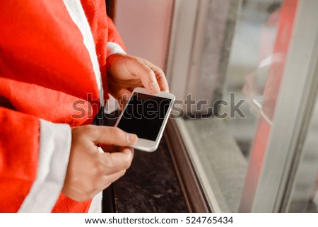 Santa Claus standing at window and using apps on a touch screen mobile phone, Christmas and technology concept