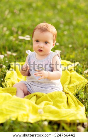 A small child, a little girl sitting on the grass, warm summer day, looking to the side, a serious look, hold in arms flower