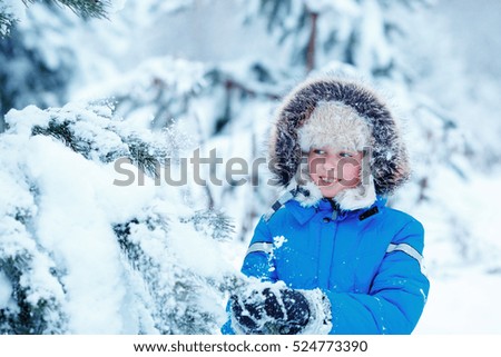 Cute little boy wearing warm clothes playing on winter forest on beautiful winter snowy day