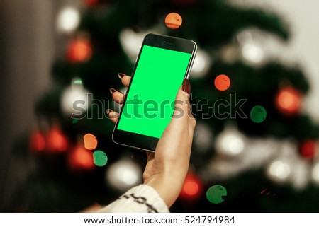 stylish woman holding phone and showing empty screen at christmas tree lights. seasonal greetings. christmas advertising concept with space for text  
