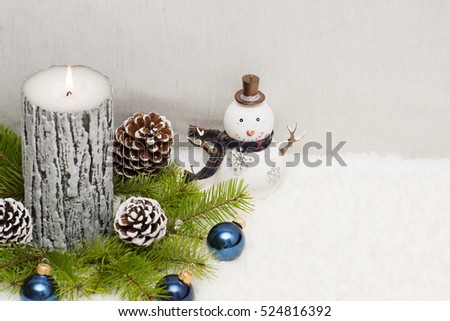 Christmas still life has the burning candle. Bright background has tree branches and different toys. 