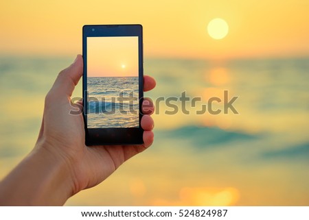 Cell technology and vacation. Close up of male hand holding smartphone, taking picture of sea sunset.