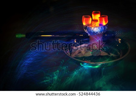 Hookah hot coals on shisha bowl with mouthpieces and color lights with dark background Royalty-Free Stock Photo #524844436