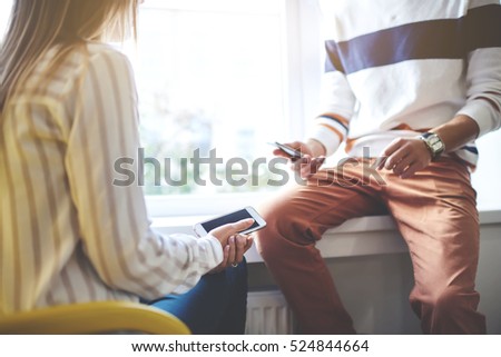 Male and female colleagues watching video and photo files in social network, checking email via modern cell phone apps connecting to fast wireless. Friends talking about new applications in store