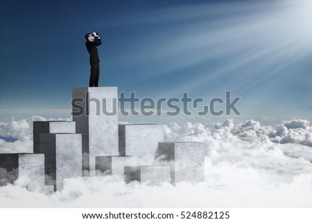 Picture of a male worker standing on the concrete wall and looking at the bright sunlight using binoculars
