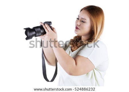 Portrait of fat woman holding a digital camera while standing in the studio, isolated on white background 