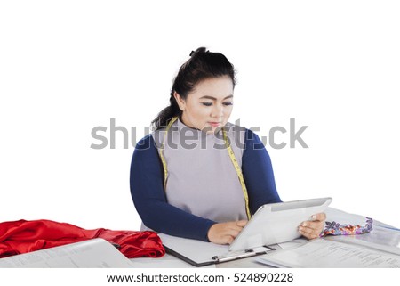 Fashion designer looking at digital tablet while sitting in the studio, isolated on white background