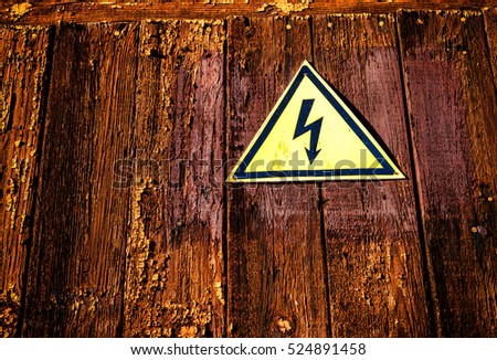 Yellow shaped electricity warning sign with a black electric bolt on a dark aged wood grunge style background.