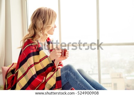 Portrait of woman basking with plaid and tea looking in window