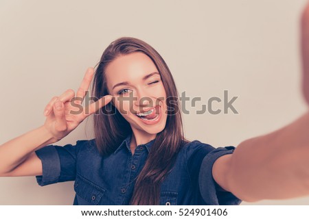 Comic girl gesturing v-sign and showing tongue while making selfie.