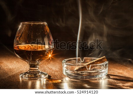 Cigar Smoking in the ashtray, cognac drinks on black background