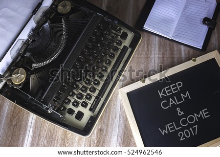 Vintage typewriter on the old wooden desk with black board writing KEEP CALM & WELCOME 2017.