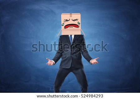 Businessman wearing cardboard box with drawn crying face on his head. on blue chalkboard background. Anonymous person. Issues of small business. Bear losses.