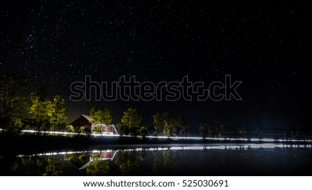 Night scene from a lake in Canada with a red barn and lights from passing cars