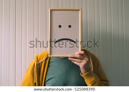 Put a sad pessimistic face on, sadness and depressive emotions concept, man holding picture frame with smiley emoticon printed. Royalty-Free Stock Photo #525088390