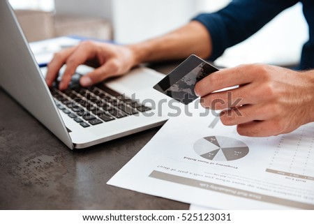 Cropped photo of young man's hands holding a credit card and typing. Online shopping on the internet using a laptop.